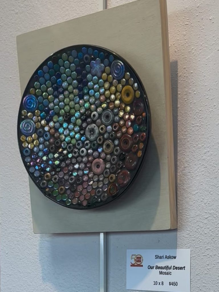 Colorful circular artwork made of various small round mixed gemstones, and mixed media materials on a metal base, mounted on wood.