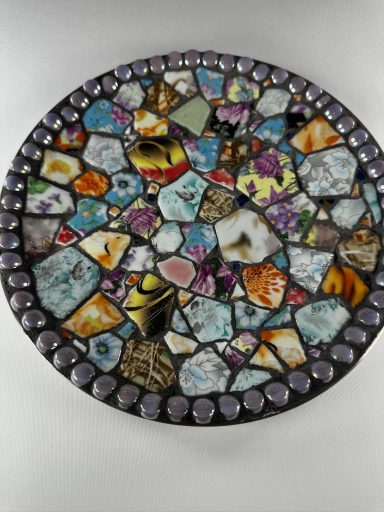 Colorful mosaic made of various stones and patterns arranged in a circular design. repurposed ceramic pottery on a stainless steel plate 
