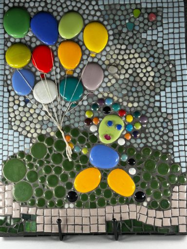 Colorful stones arranged to depict a child holding balloons in a vibrant landscape.