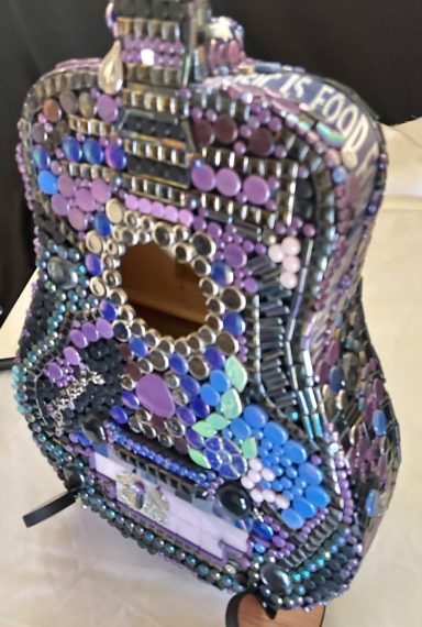 A colorful, embellished guitar covered in various decorative materials.